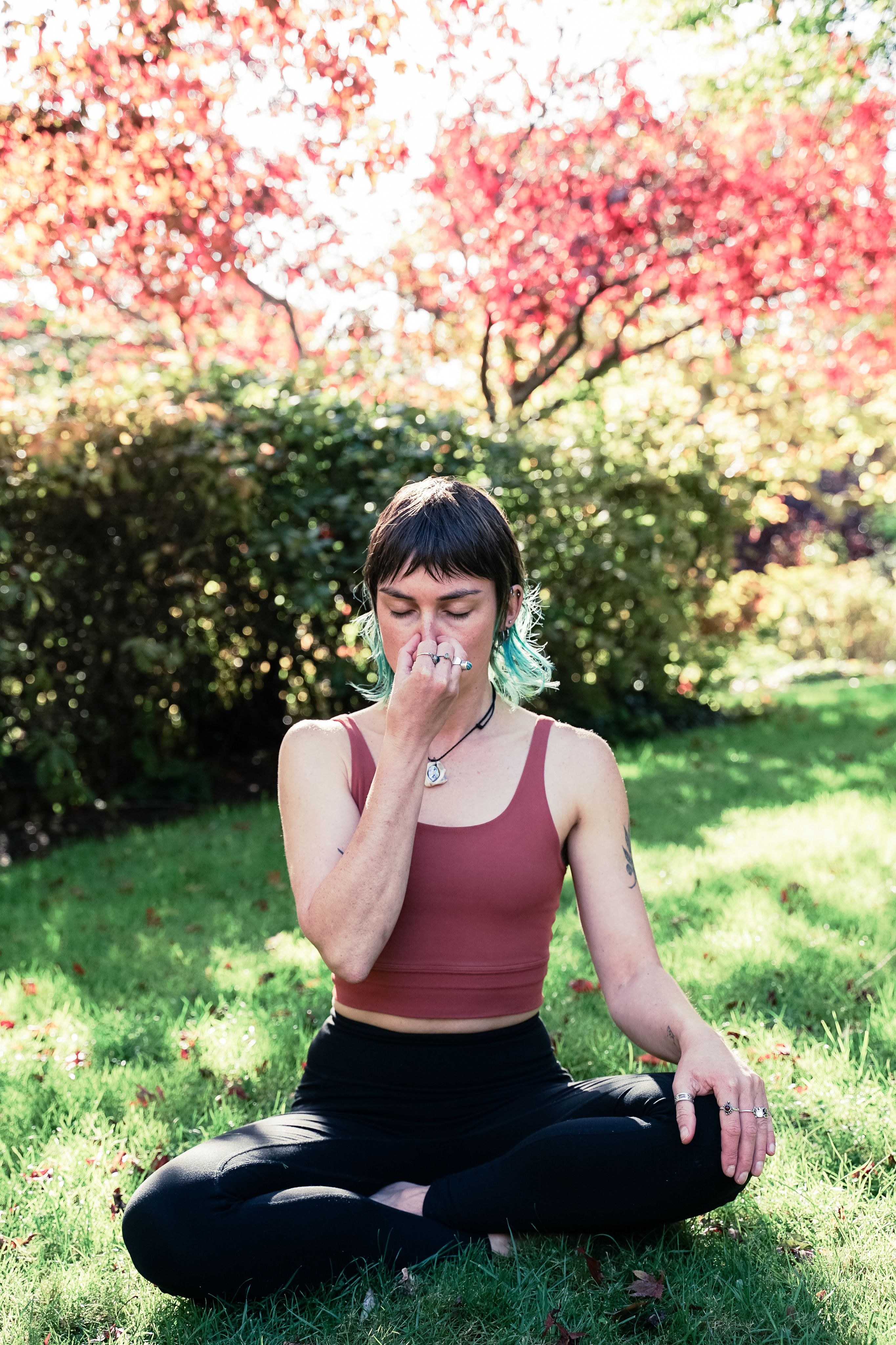 Becca, eyes closed, holding her nose with her thumb and pinky finger, while sitting on grass.
