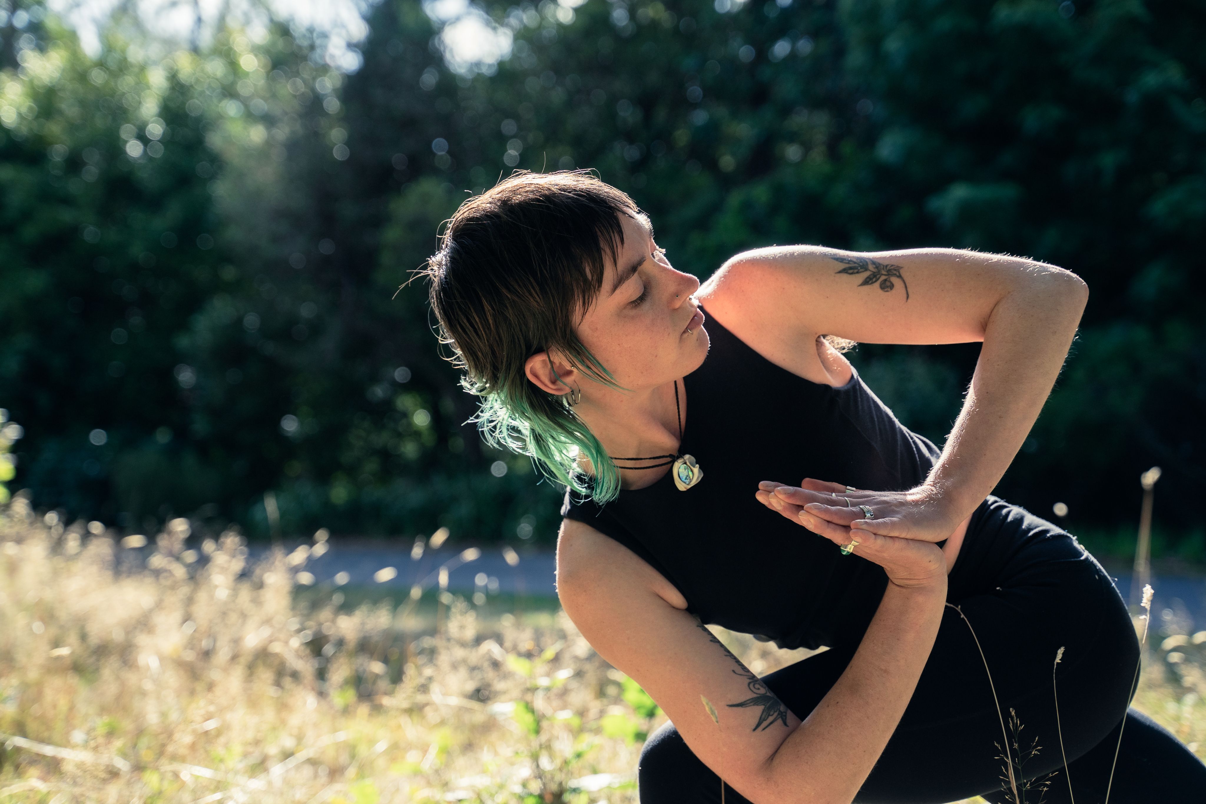 Becca twisting her upper body with her elbow locked over her knee, while her palms are together.